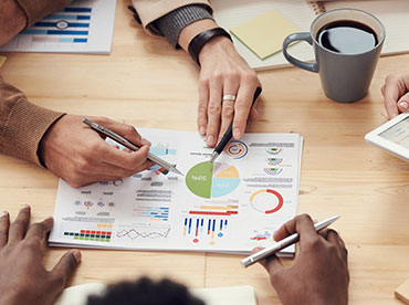 three people reviewing documents on a table with a cup of coffee